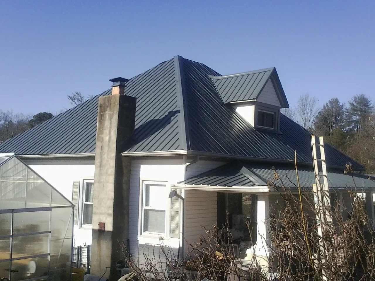 Dark blue standing seam metal roof on a white farmhouse with dormer — Slate & Tile Roof Repair by Roofing Brothers in Brookside