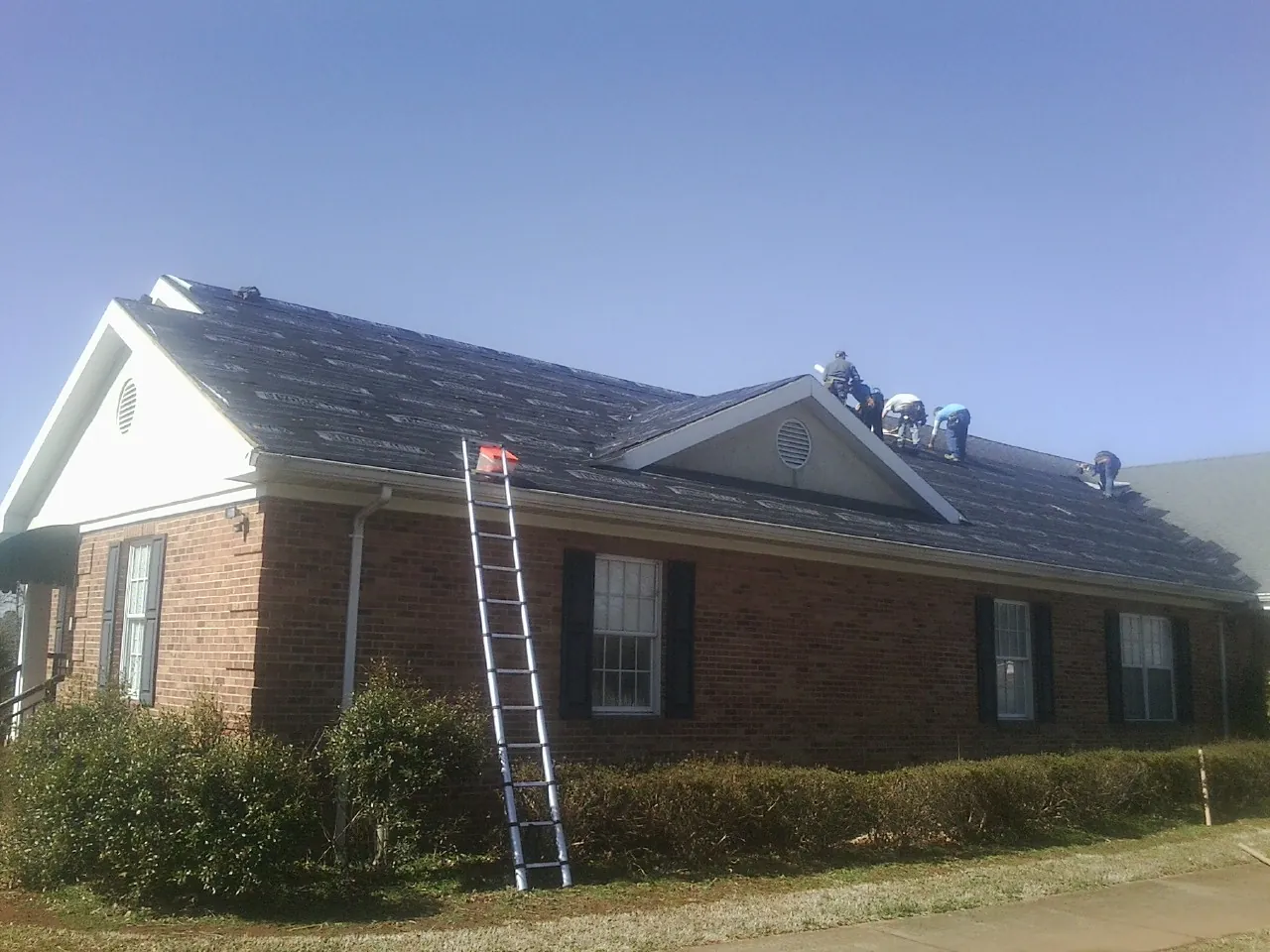 Crew tearing shingles off a brick ranch roof with a ladder set — Emergency Roof Repair work by our crew in Brookside