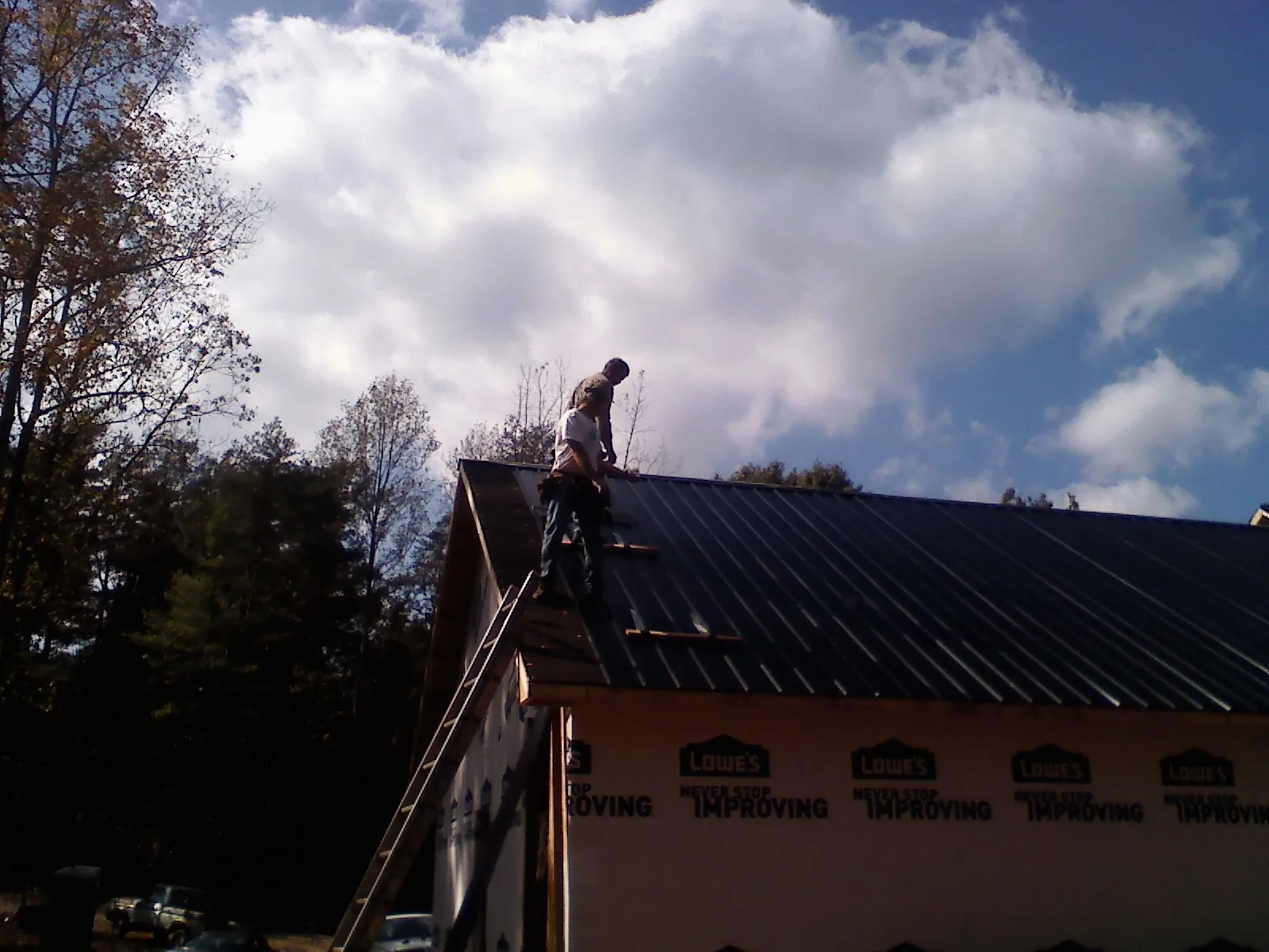 Roofer fastening dark metal panels high against a cloudy sky, from a Roof Inspection job in Brookside