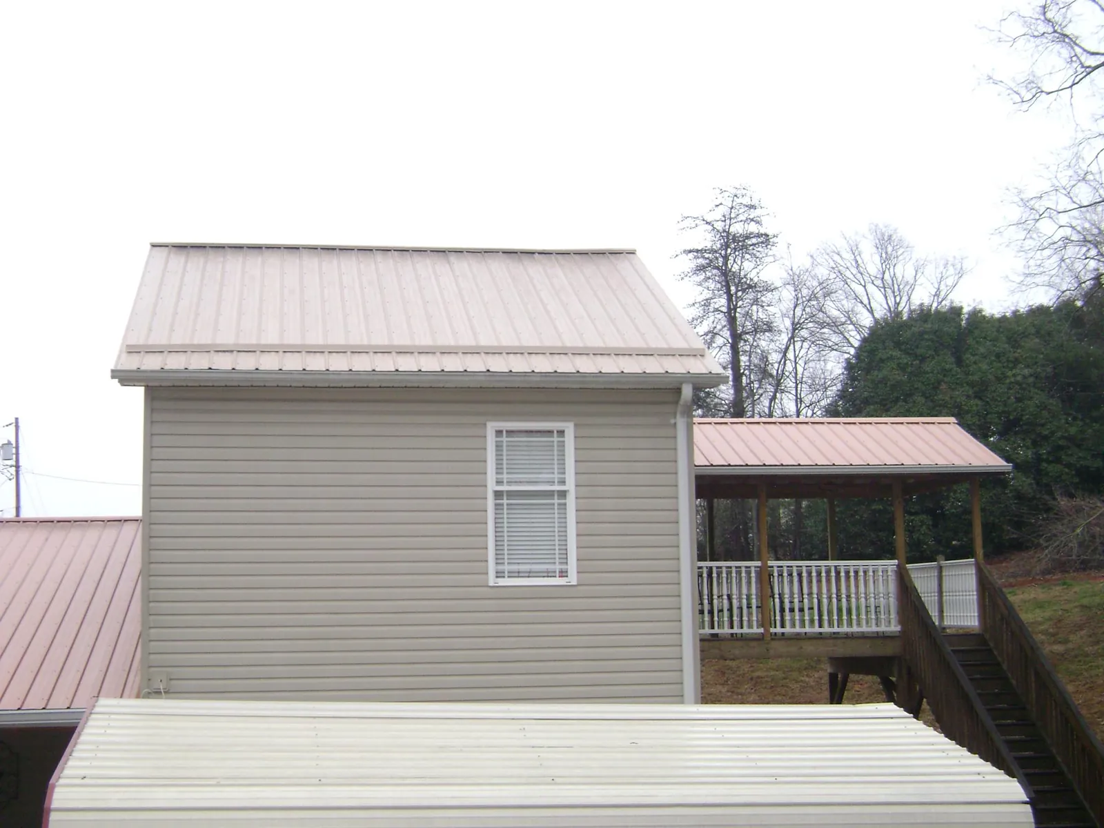 Tan metal roofs on a two story addition and attached porch, from a Roof Replacement job in Brookside
